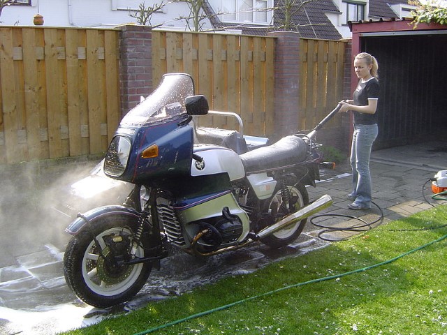 Eine Frau reinigt das Motorrad mit einem Hochdruckreiniger