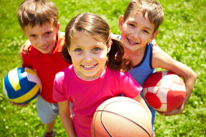 Drei Kinder stehen mit einem Ball auf der Wiese