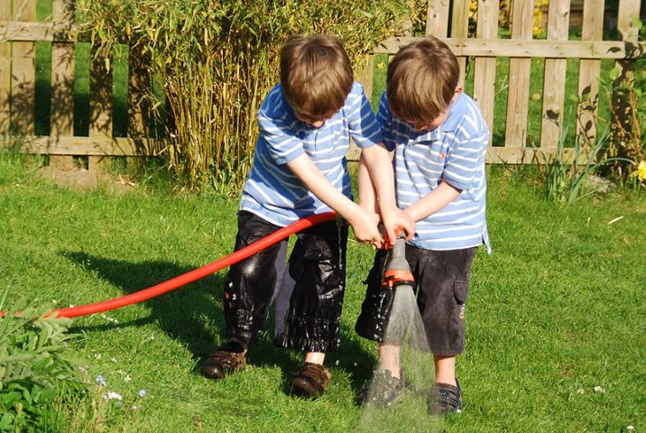 Zwillinge spielen mit Wasser auf der Wiese